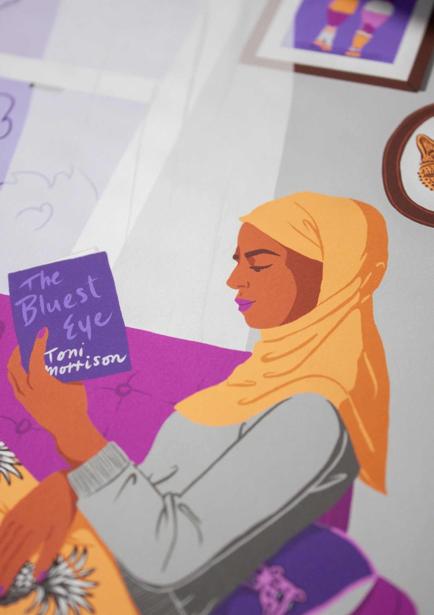 Close-up of an illustration of a Muslim woman reading the book The Bluest Eye by Toni Morrison. She is sat by the window on an armchair and the light curtains are being moved by the breeze.