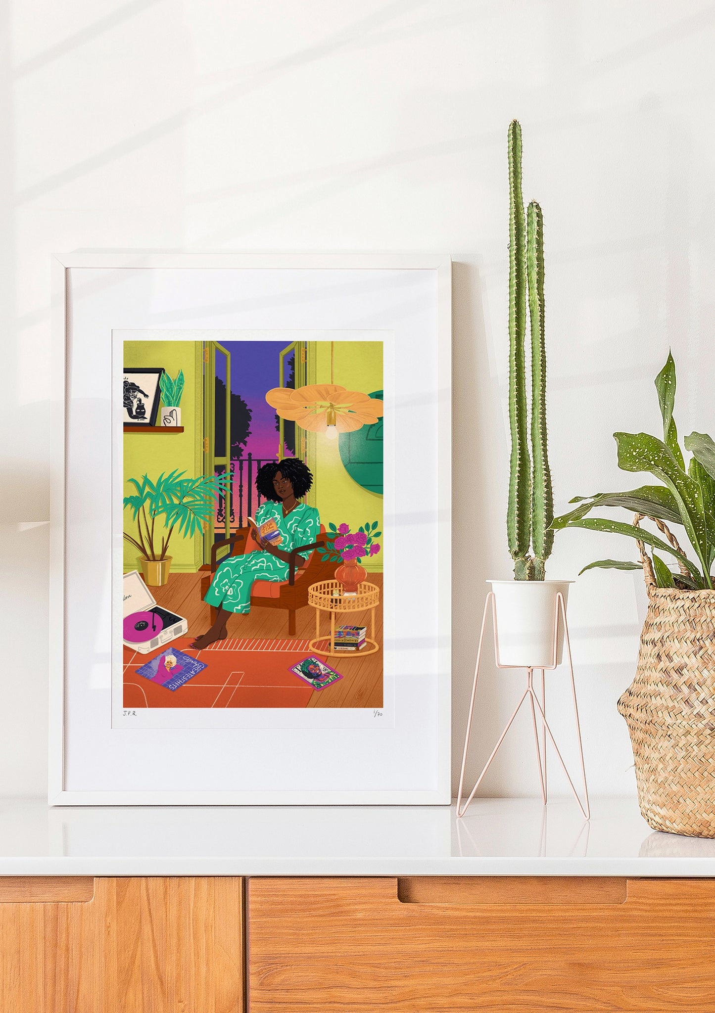 Framed illustration of a Black woman reading the book In Spite of Oceans by Huma Qureshi. She is sat by the opened door giving out to a sunset and she is surrounded by books, magazines, and vinyls.